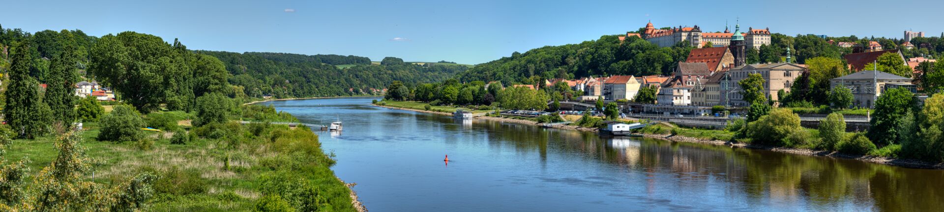 Eine Landschaft mit einem Fluss, Bäumen und einem blauen Himmel.